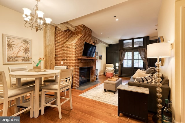 living area featuring wood finished floors, a brick fireplace, and a chandelier