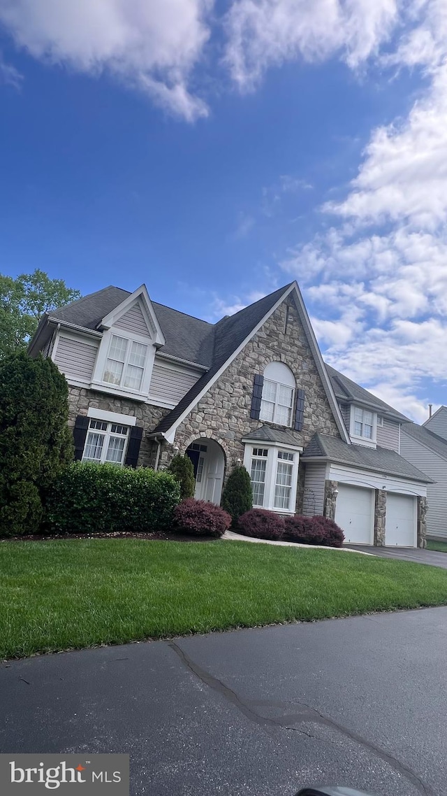 view of front facade featuring stone siding, a front lawn, and asphalt driveway