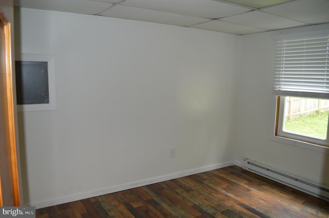 unfurnished room with a paneled ceiling, a baseboard heating unit, dark wood-style flooring, baseboards, and electric panel