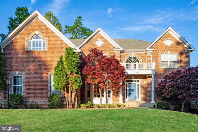 colonial inspired home featuring a balcony, brick siding, and a front yard