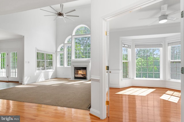 unfurnished living room featuring ceiling fan, a fireplace with flush hearth, healthy amount of natural light, crown molding, and a high ceiling