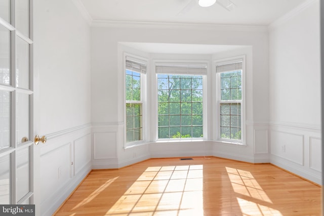 unfurnished room featuring light wood-type flooring, a wainscoted wall, ornamental molding, and ceiling fan
