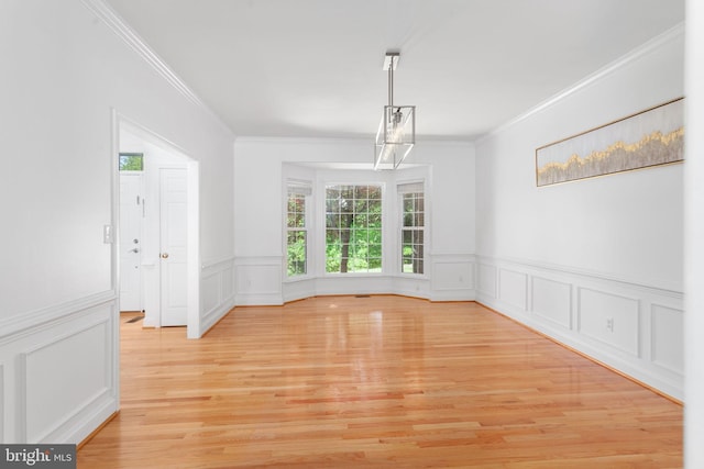 unfurnished dining area featuring crown molding, healthy amount of natural light, a decorative wall, light wood-style flooring, and a wainscoted wall
