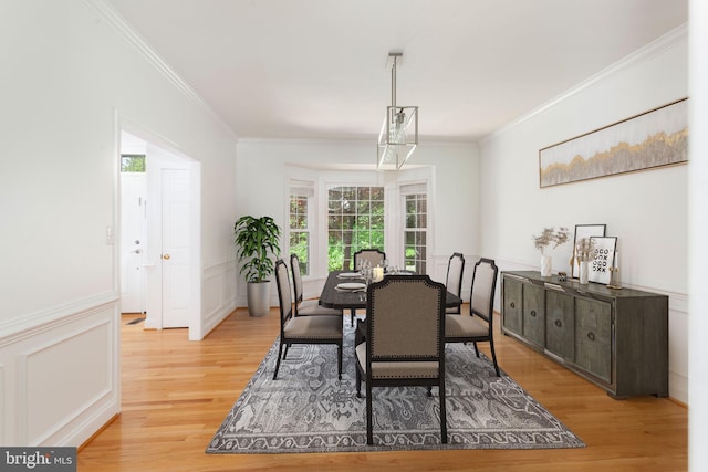 dining space featuring crown molding, light wood-style flooring, plenty of natural light, wainscoting, and a decorative wall