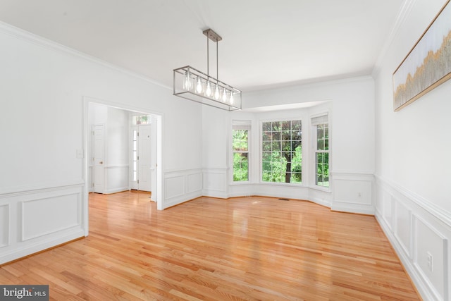 unfurnished dining area with light wood-style floors, ornamental molding, a decorative wall, and wainscoting