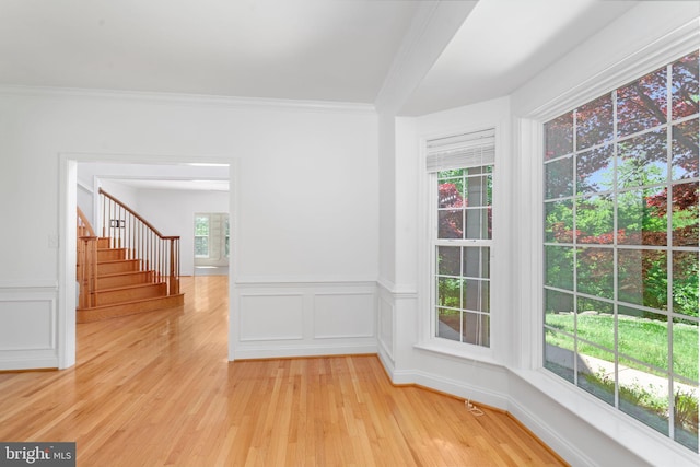 spare room featuring healthy amount of natural light, stairway, light wood-type flooring, ornamental molding, and wainscoting