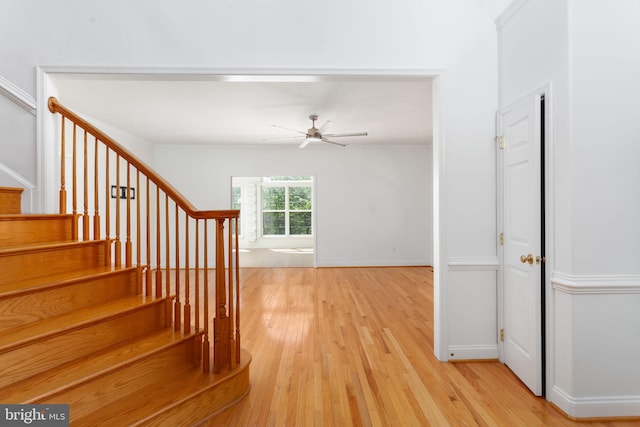 stairway with wood finished floors, a ceiling fan, and baseboards