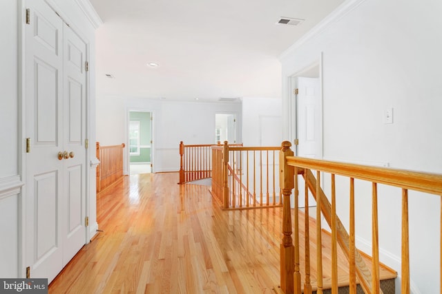 corridor with an upstairs landing, light wood finished floors, and ornamental molding