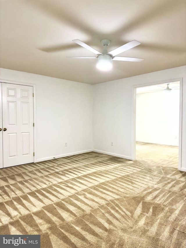 carpeted empty room with a ceiling fan and baseboards