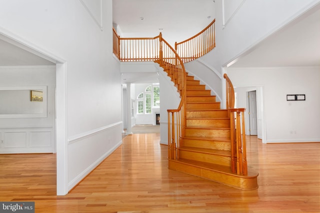 staircase featuring a towering ceiling, wood finished floors, baseboards, and crown molding