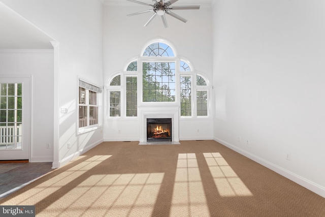unfurnished living room with a towering ceiling, carpet, a fireplace with flush hearth, ceiling fan, and baseboards