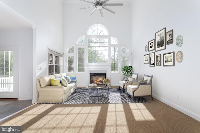 living area with a high ceiling, a glass covered fireplace, healthy amount of natural light, and ceiling fan
