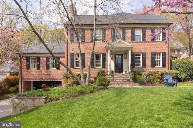 georgian-style home featuring brick siding, a front lawn, and a chimney