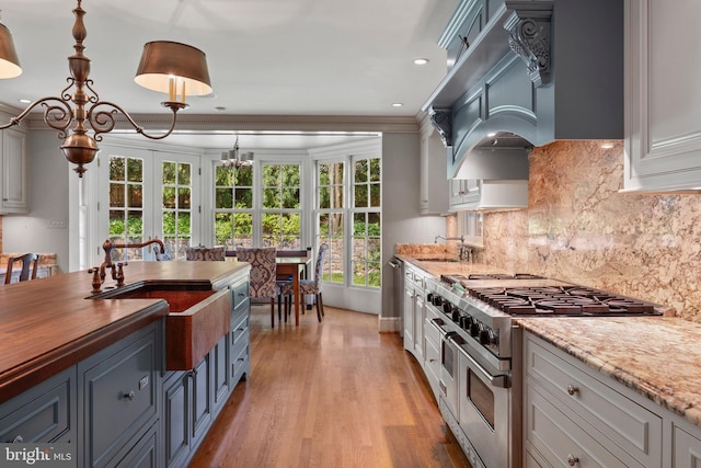 kitchen with range with two ovens, light wood-style flooring, backsplash, recessed lighting, and hanging light fixtures