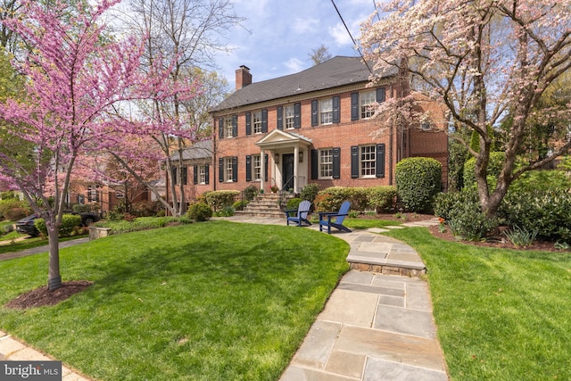 view of front facade with brick siding, a chimney, and a front lawn