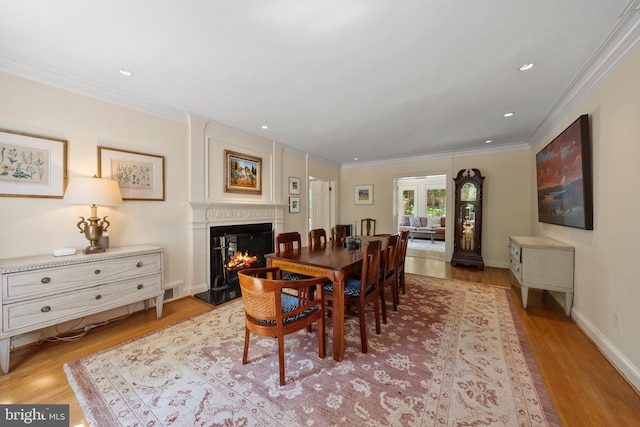 dining room featuring light wood-type flooring, a glass covered fireplace, ornamental molding, baseboards, and recessed lighting