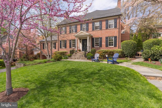 colonial-style house featuring brick siding, a chimney, and a front yard