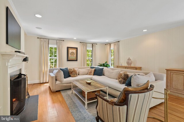 living area featuring light wood-style floors, a lit fireplace, crown molding, and recessed lighting