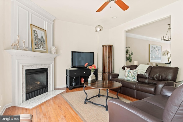 living room featuring wood finished floors, ceiling fan, a premium fireplace, ornamental molding, and baseboards