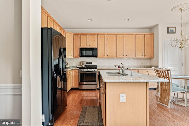 kitchen with black appliances, a sink, light brown cabinetry, light wood-style floors, and a center island with sink