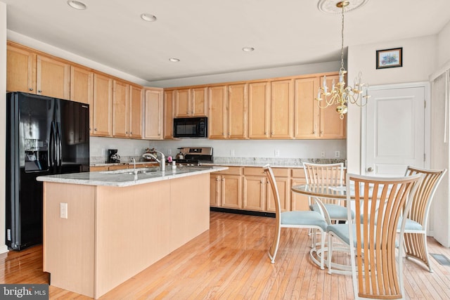 kitchen with black appliances, light brown cabinetry, a chandelier, light wood-style floors, and an island with sink