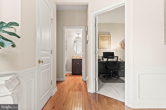 hall with a desk, light wood-type flooring, and a sink