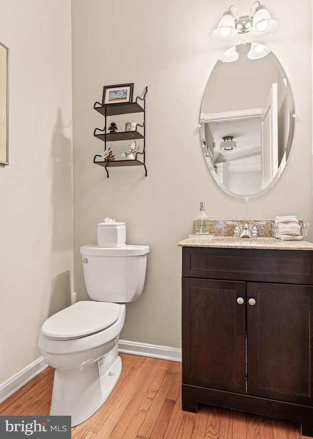 half bathroom with baseboards, wood finished floors, toilet, and vanity