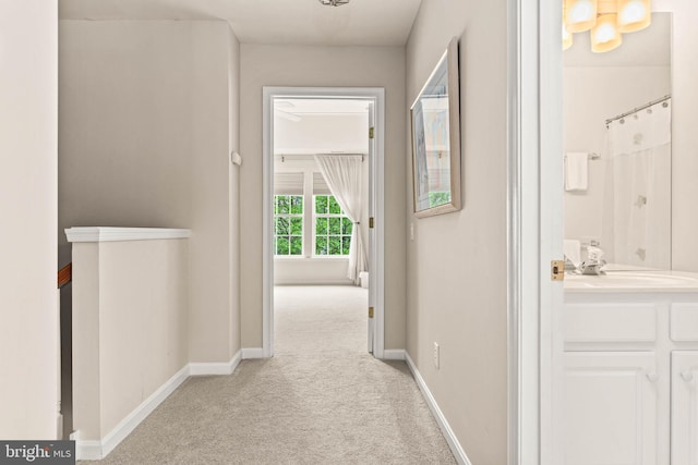 hallway with light carpet, baseboards, and a sink