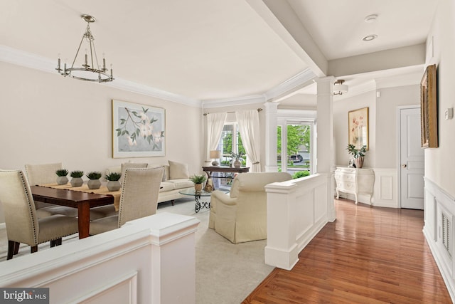 living area with crown molding, ornate columns, light wood finished floors, a wainscoted wall, and a decorative wall