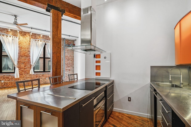 kitchen with stainless steel counters, island exhaust hood, black electric stovetop, oven, and brick wall