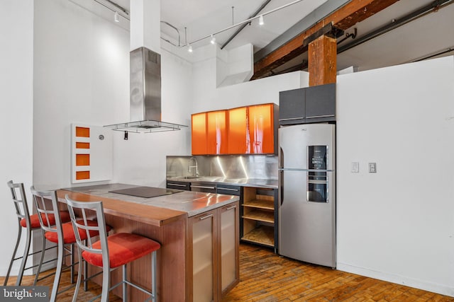 kitchen featuring stainless steel counters, freestanding refrigerator, rail lighting, island exhaust hood, and a high ceiling