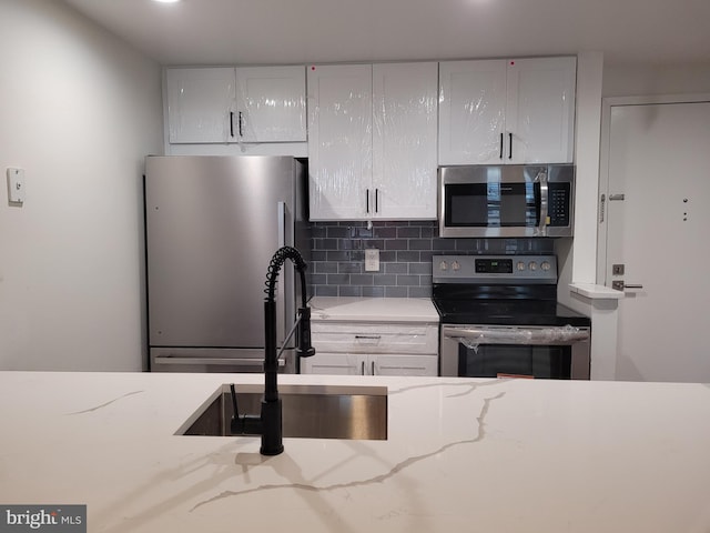 kitchen with stainless steel appliances, a sink, decorative backsplash, and white cabinetry