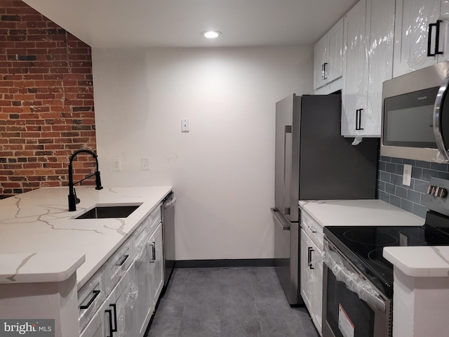 kitchen with stainless steel appliances, a sink, white cabinetry, backsplash, and light stone countertops