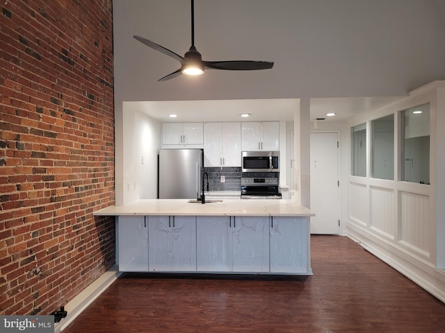 kitchen featuring stainless steel appliances, a sink, brick wall, a ceiling fan, and a peninsula