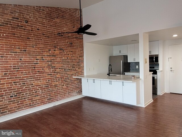 kitchen with appliances with stainless steel finishes, a ceiling fan, a sink, dark wood finished floors, and brick wall