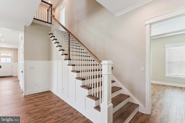 stairway with wood finished floors and crown molding