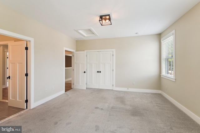 unfurnished bedroom featuring a closet, carpet, attic access, and baseboards