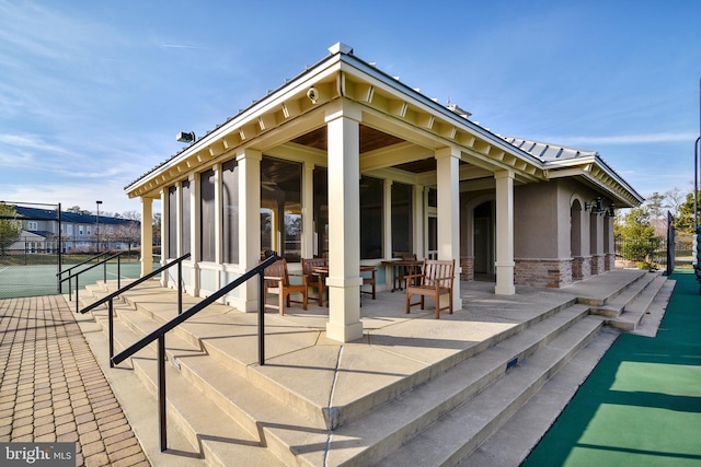 rear view of house featuring fence, a patio area, stone siding, stucco siding, and a tennis court