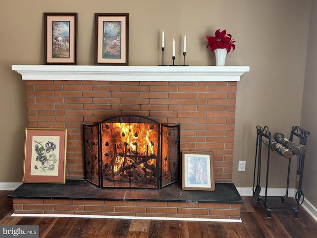 detailed view of wood finished floors, a brick fireplace, and baseboards