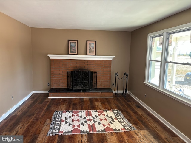 unfurnished living room with wood finished floors, a brick fireplace, and baseboards