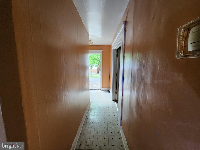 hall featuring tile patterned floors, baseboards, and wooden walls