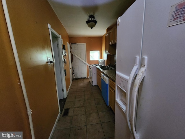 kitchen featuring white appliances, dark countertops, dark tile patterned floors, baseboards, and a sink