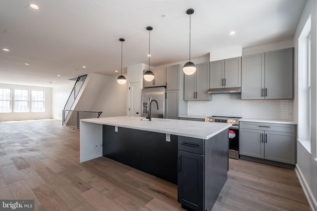 kitchen with appliances with stainless steel finishes, gray cabinetry, under cabinet range hood, tasteful backsplash, and wood finished floors