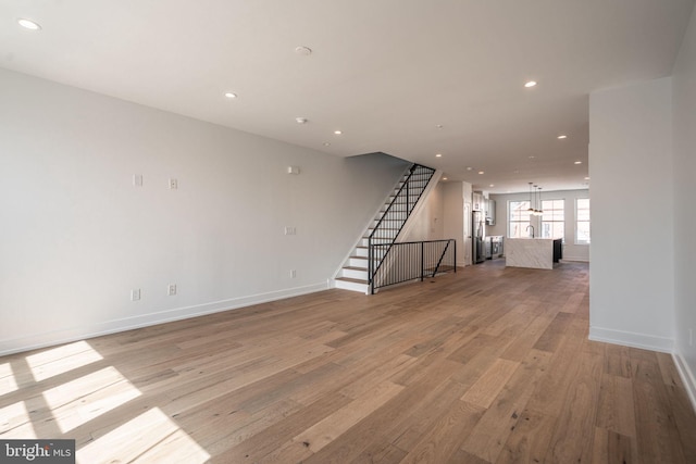 unfurnished living room with light wood-type flooring, stairs, recessed lighting, and baseboards