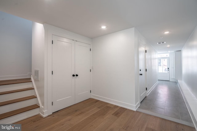hall with wood finished floors, baseboards, recessed lighting, and stairway