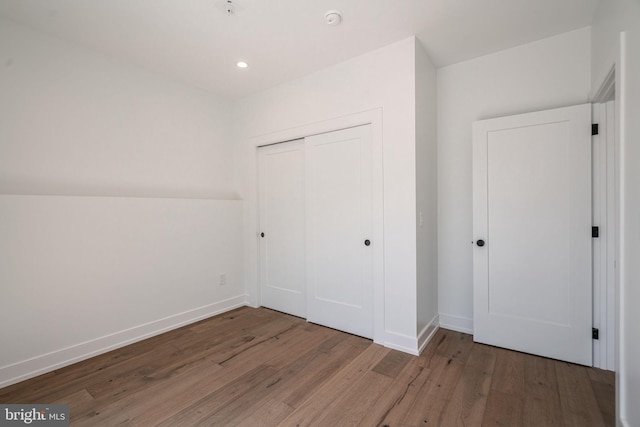 unfurnished bedroom featuring wood finished floors, a closet, baseboards, and recessed lighting