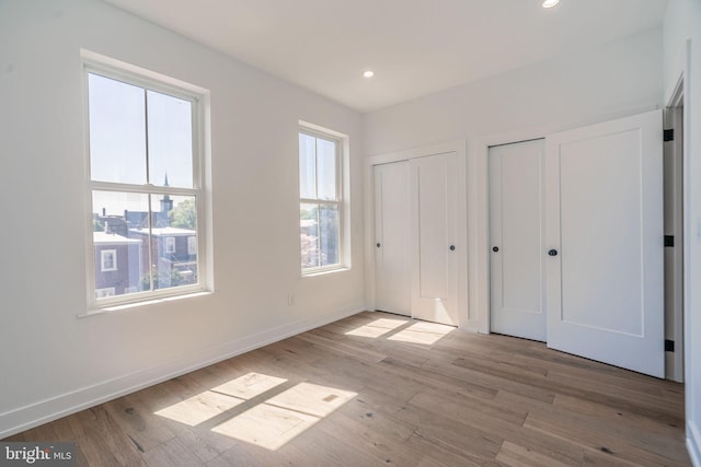 unfurnished bedroom with two closets, wood finished floors, recessed lighting, and baseboards