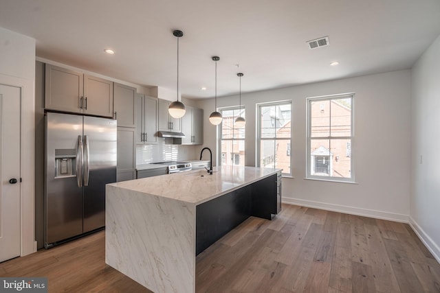kitchen with stainless steel appliances, gray cabinetry, light stone countertops, wood finished floors, and a sink