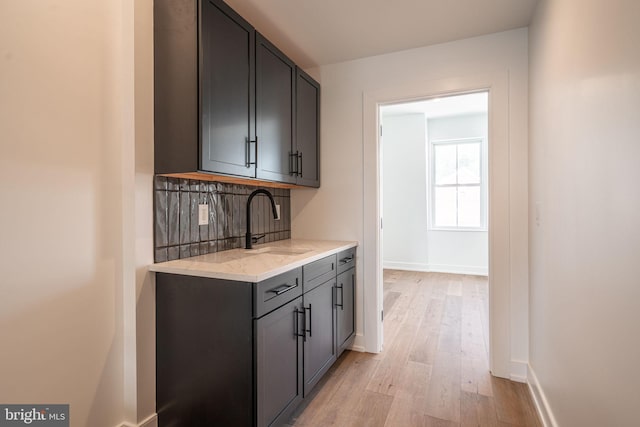 bar with light wood-type flooring, a sink, baseboards, and backsplash