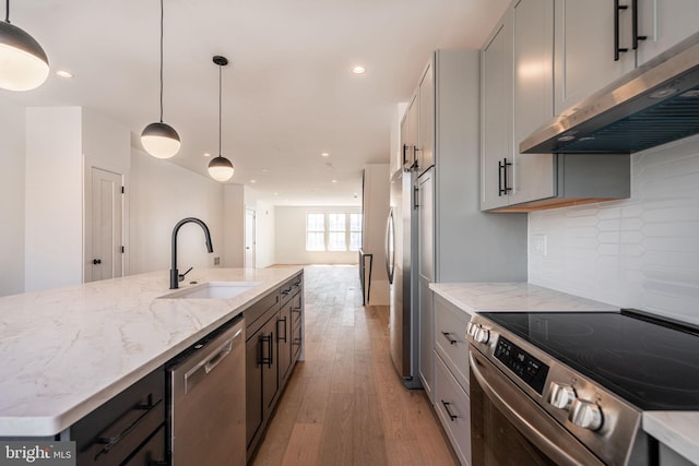 kitchen with appliances with stainless steel finishes, a sink, under cabinet range hood, light wood-style flooring, and light stone countertops